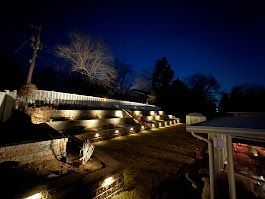 Nighttime view of a tiered brick wall with pathway lights illuminating the steps, against a dark blue sky.
