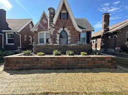 Brick Tudor-style house with arched doorway and raised brick planter in front.