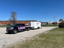 Black truck towing a white trailer on a sunny day in an empty lot.