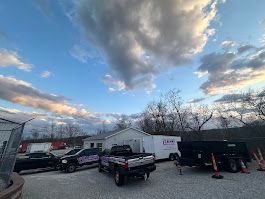 Vehicles parked in front of a white building with a cloudy sky backdrop.