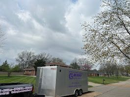 Silver trailer with company logo parked on a street with houses and trees under a cloudy sky.