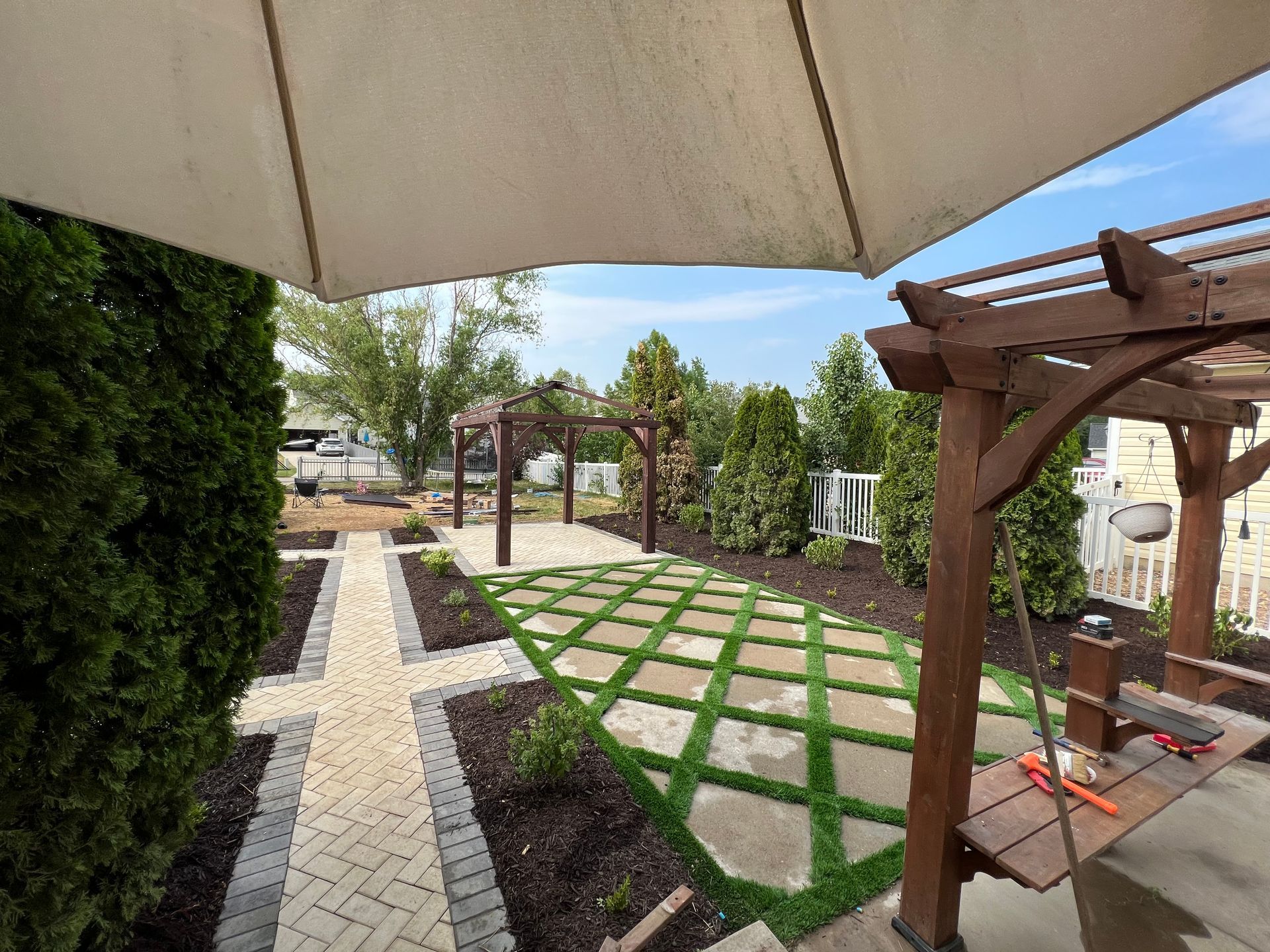 A backyard patio with a pergola, stone pathway, and a grass and stone grid pattern.