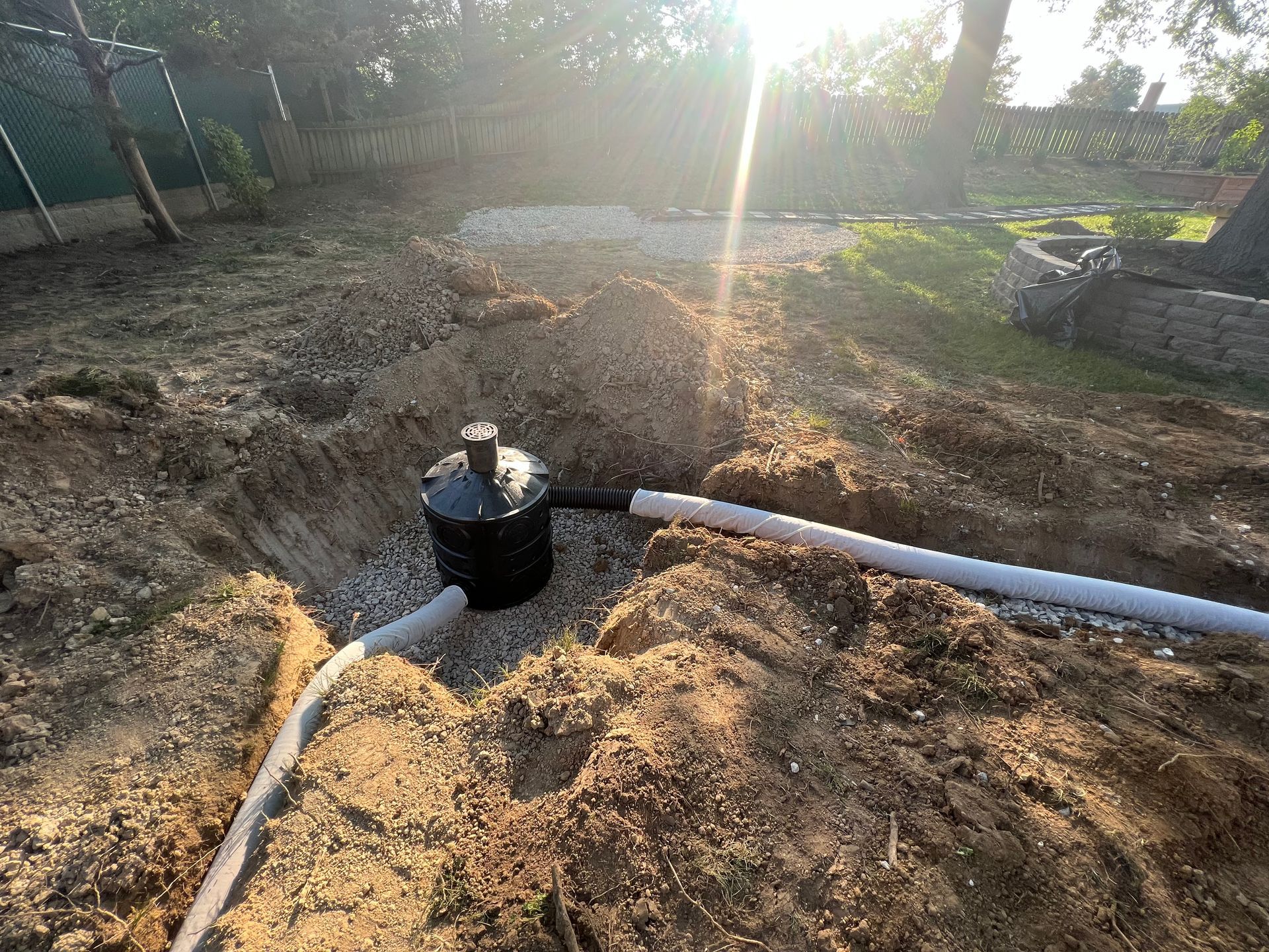 A black septic tank installation in a dug-out hole, with piping and gravel, in a yard.
