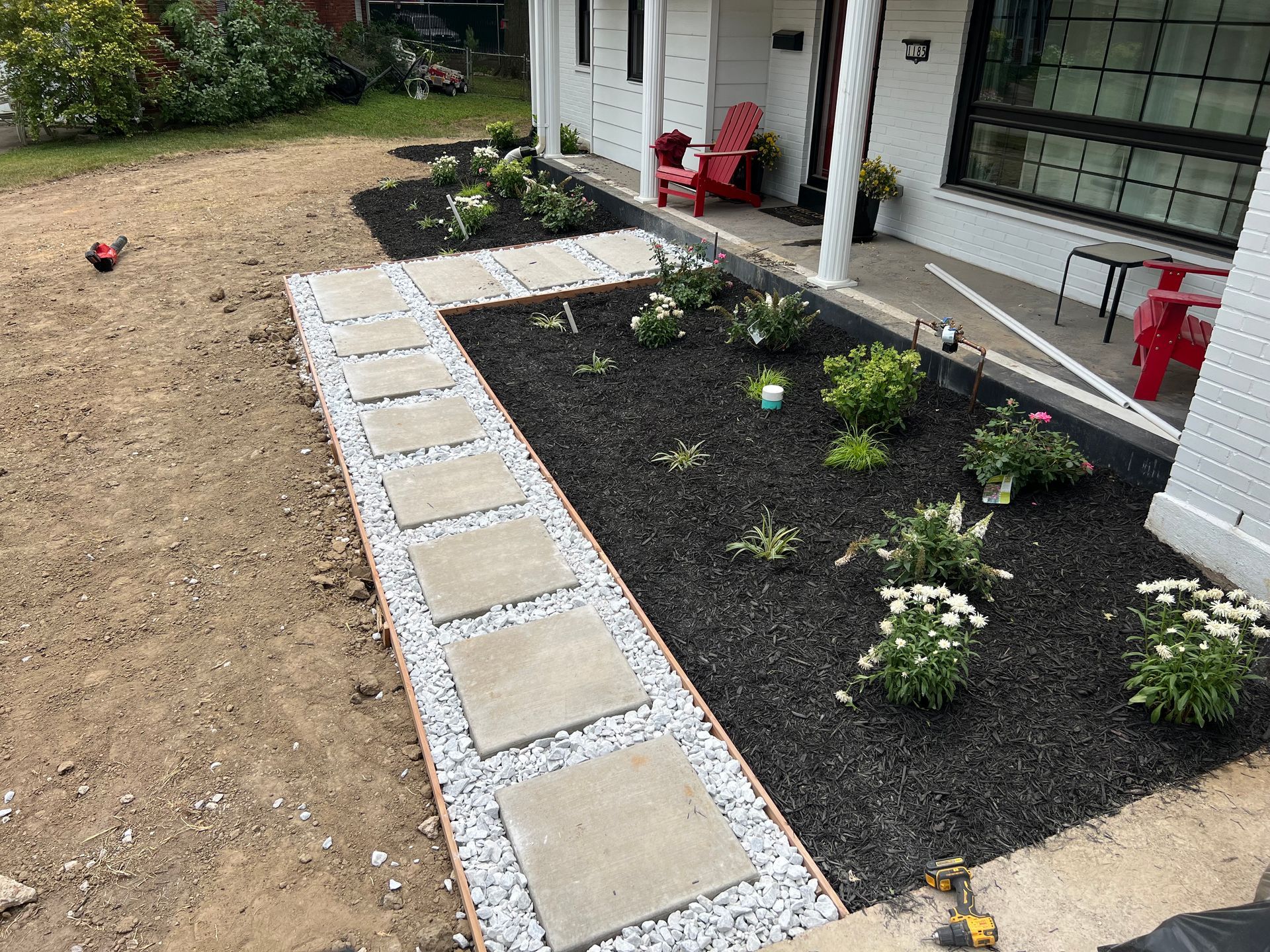 Pathway with square pavers, bordered by white gravel and dark mulch garden beds.