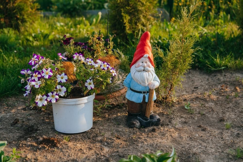 A Garden Gnome is Standing Next to a Pot of Flowers — Blue River Landscape Supplies in Foulden, QLD