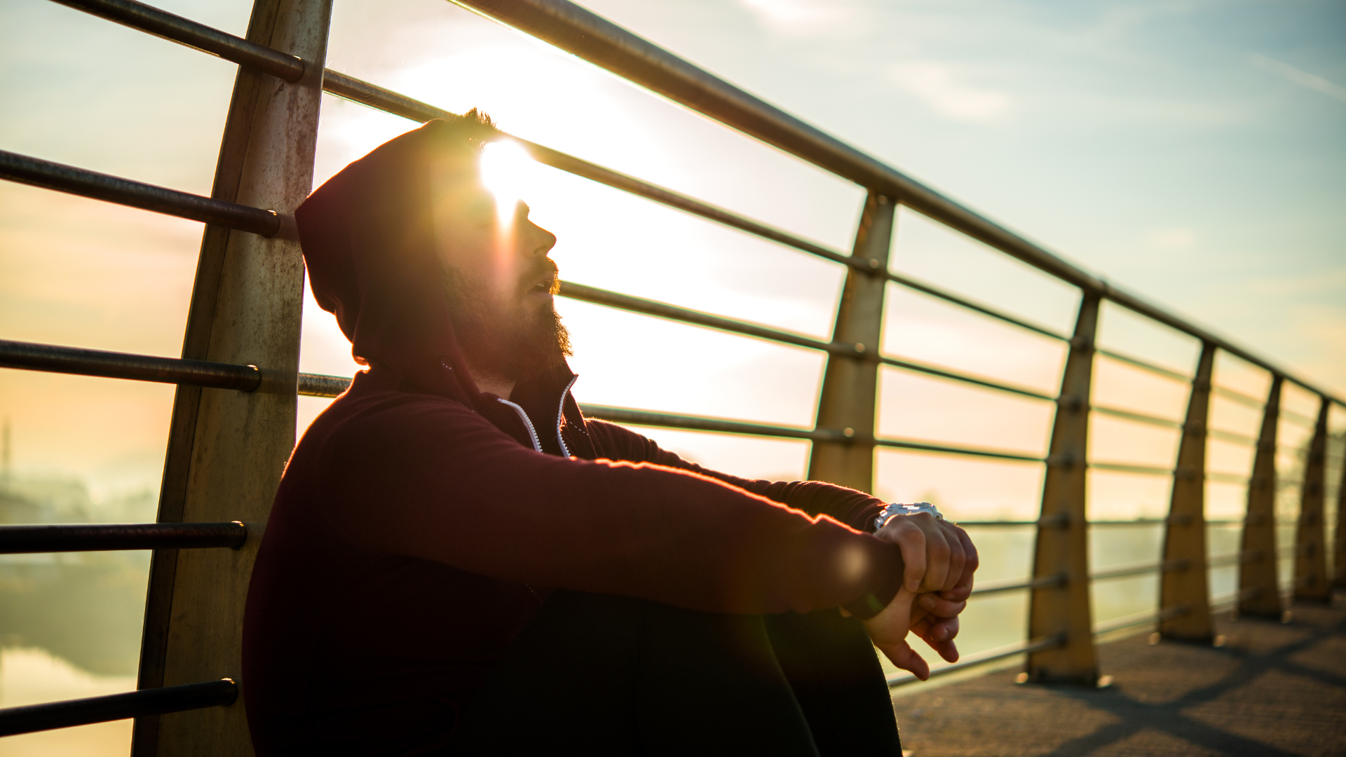 A man is sitting on a bridge looking at the sun.