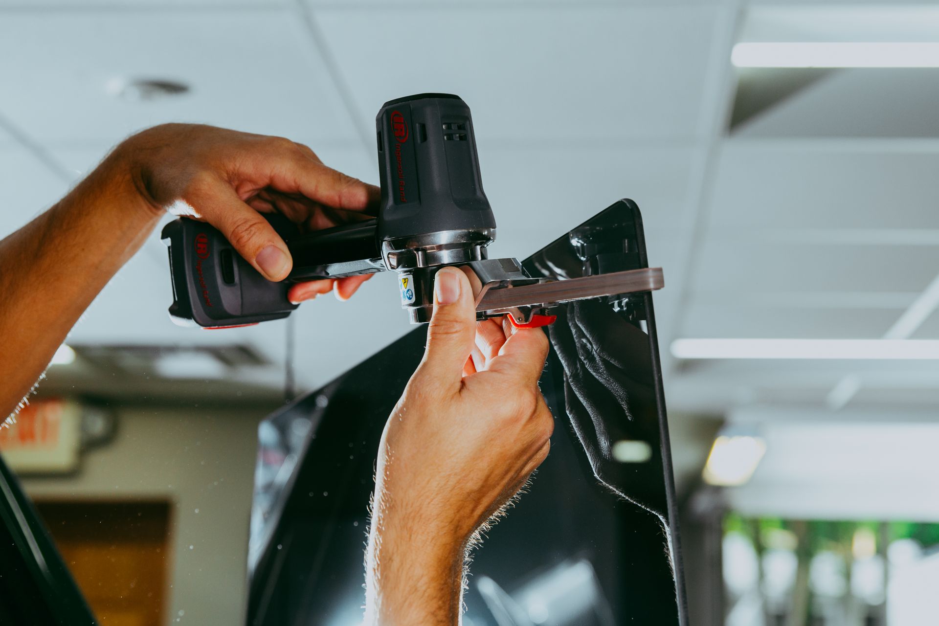 Person using a black power tool on a dark surface, possibly applying film in a shop.