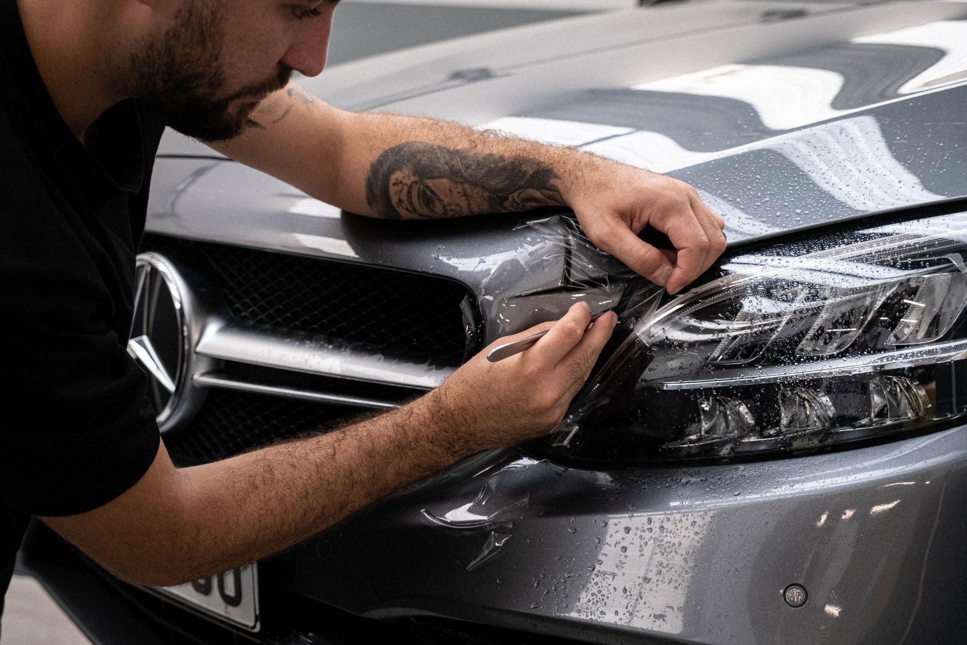 Man installing protective film on a car's headlight. Gray Mercedes.