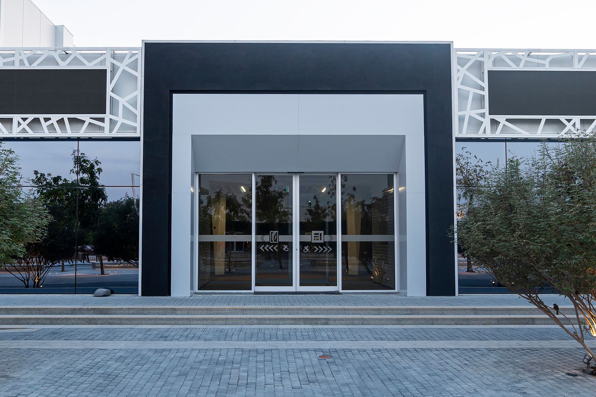 Entrance to modern building with glass doors, gray facade, and decorative white panels.