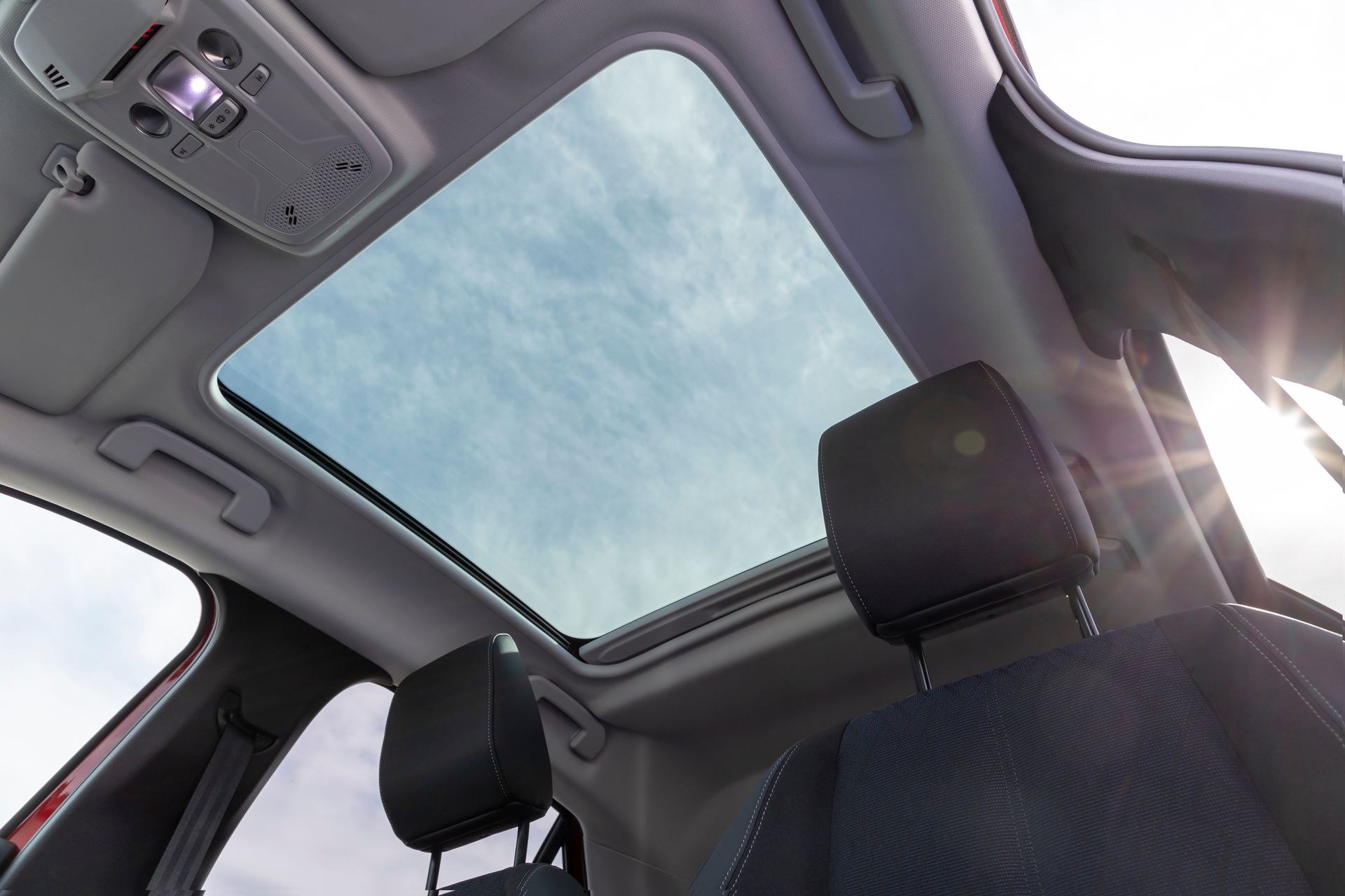 Interior car view with open sunroof, blue sky, and black headrests.