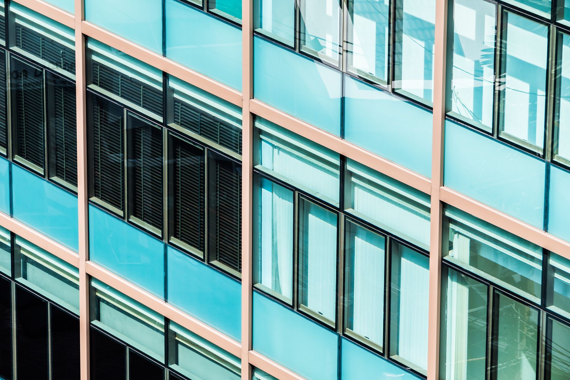 Close-up of a modern building facade with rows of turquoise windows and beige frames.