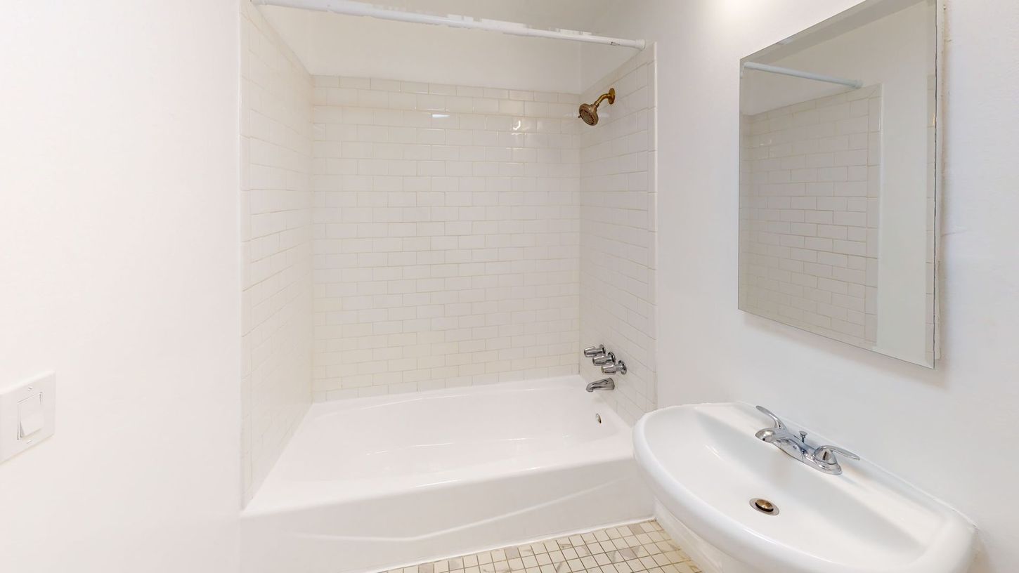 White bathroom with a tub, sink, and mirror. White tiled shower surround.