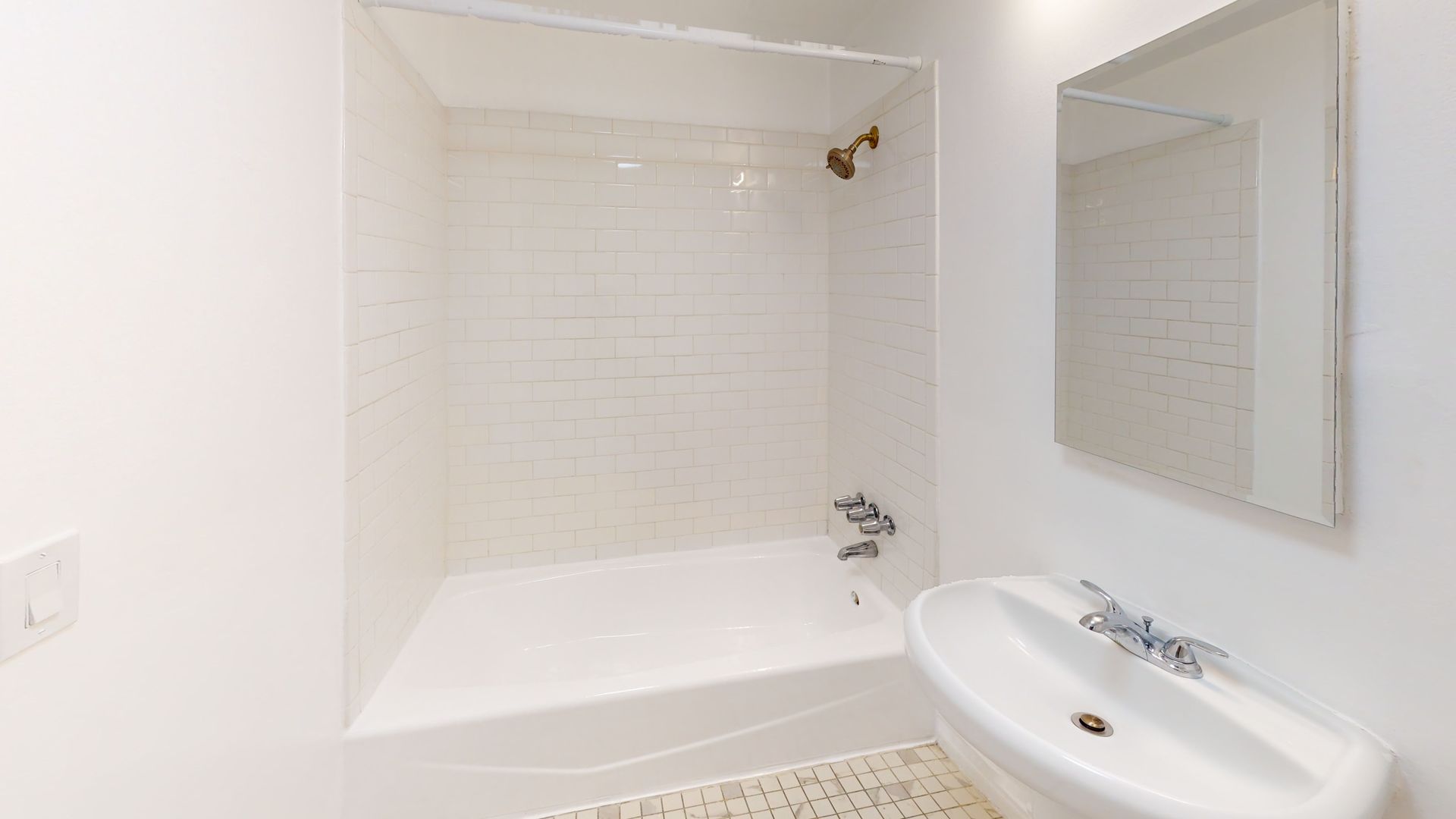 White bathroom with a tub, sink, and mirror. White tiled shower surround.