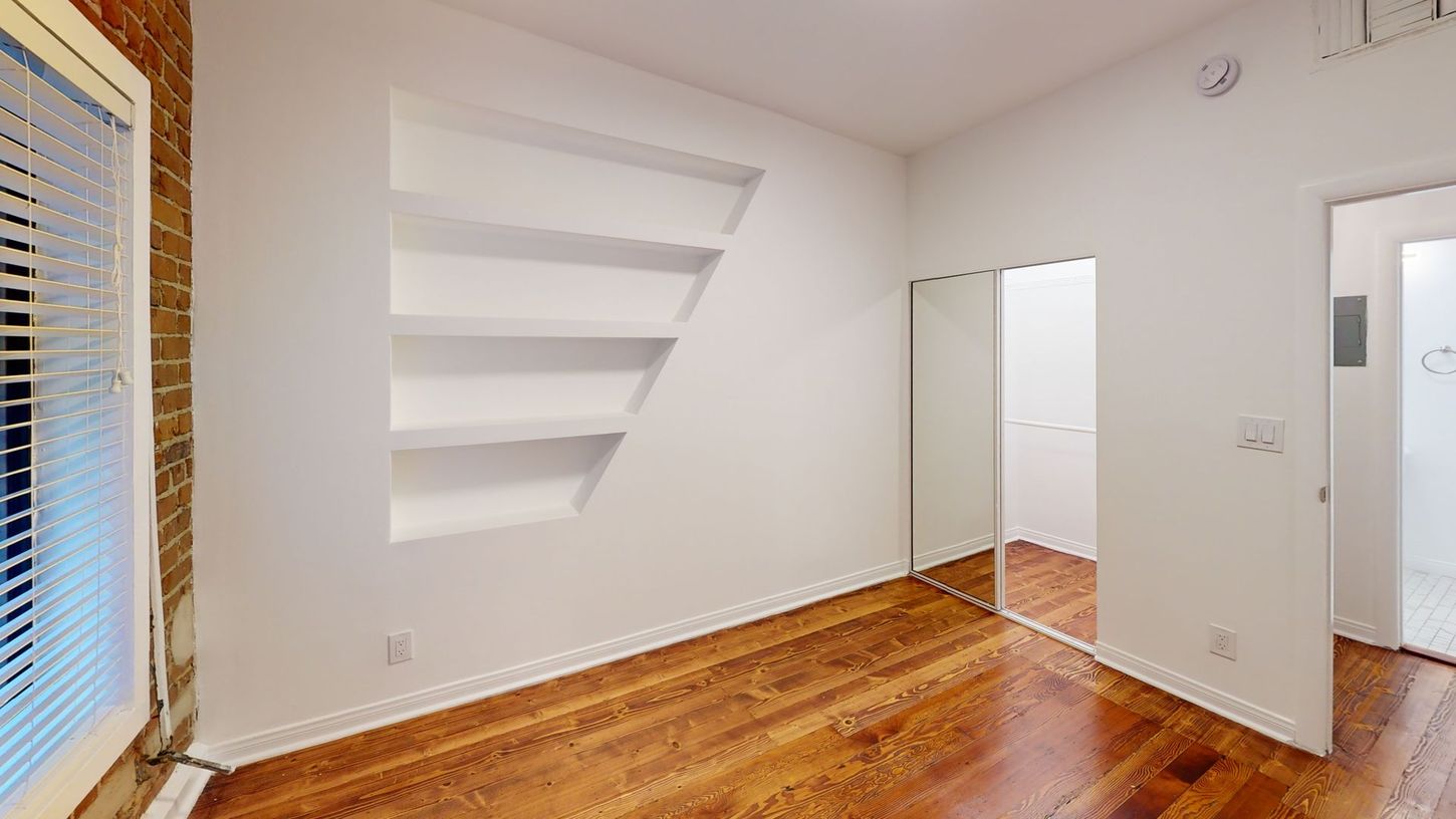 Empty room with built-in shelves, hardwood floors, and a doorway to another room.