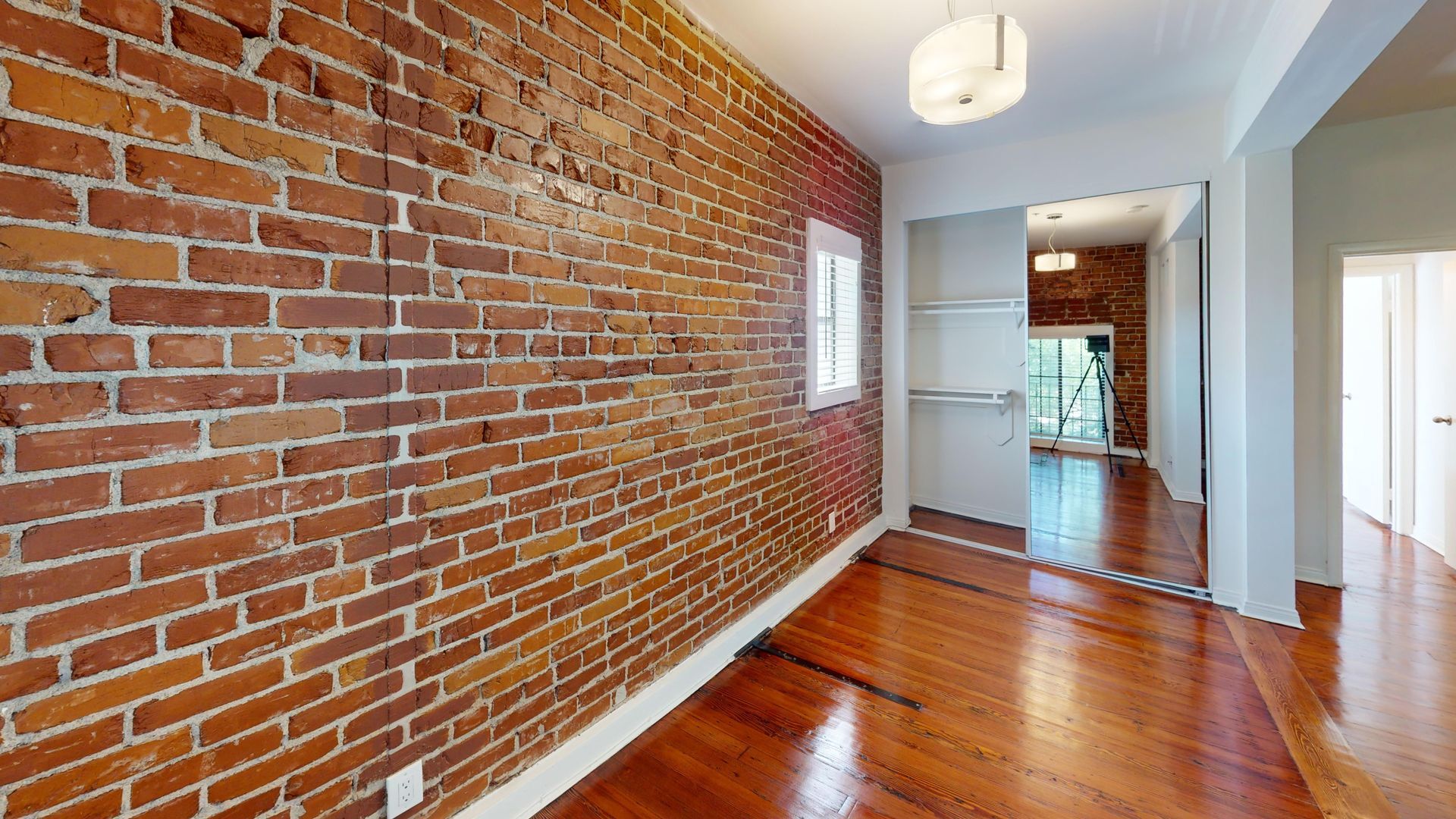 Interior room with exposed brick wall and hardwood floor. Doorway to another room.
