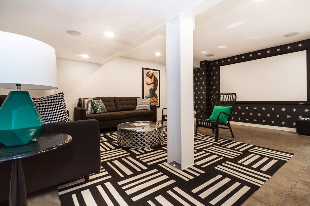Basement living room with a screen, seating, patterned rug, and a geometric lamp.