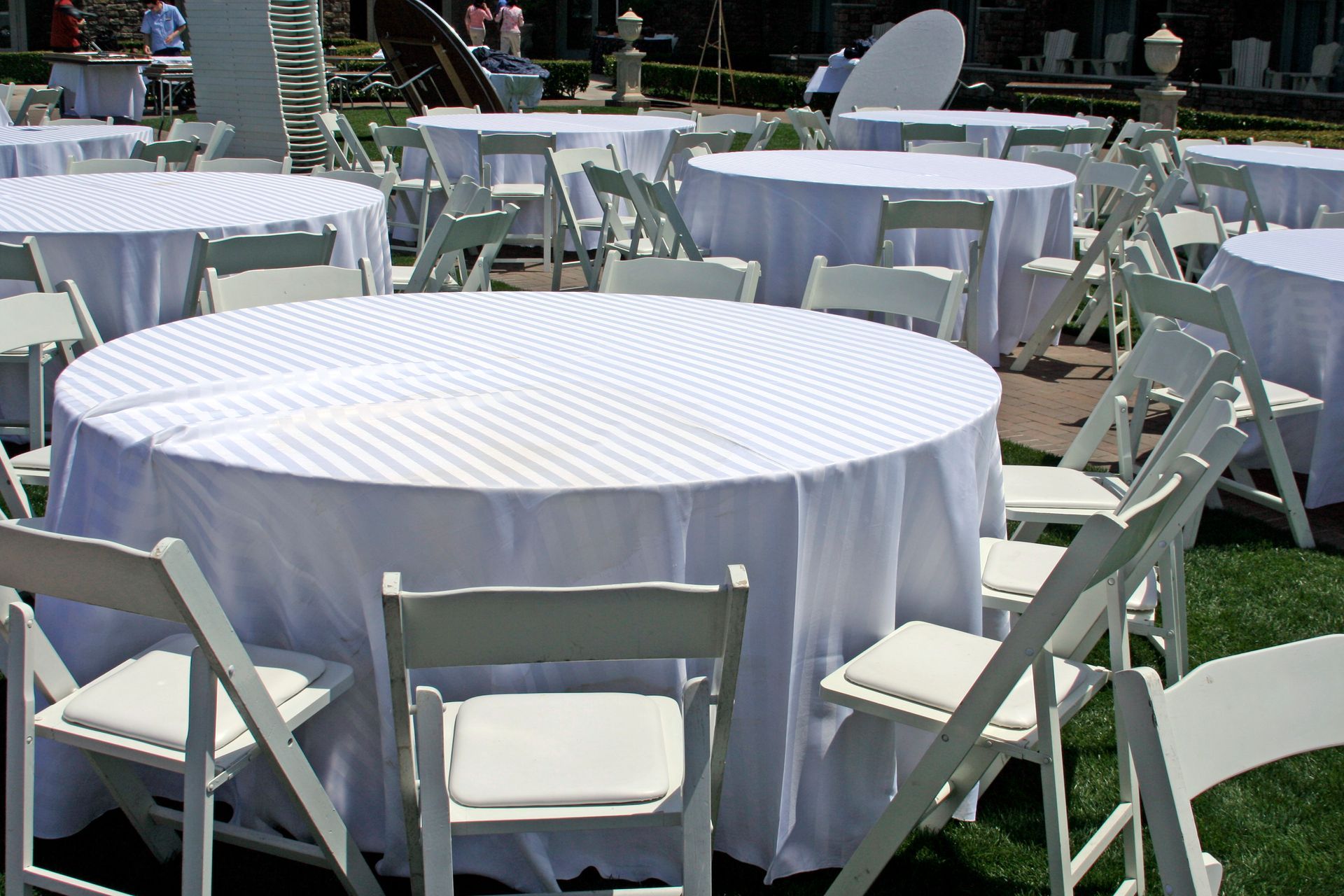Outdoor event setup with round tables covered in white linens and arranged white folding chairs.
