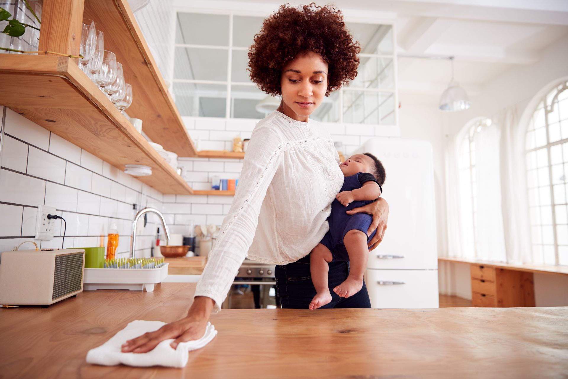 Woman with baby cleaning a kitchen counter.