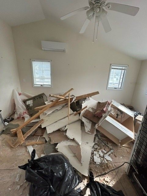 A room with a lot of trash on the floor and a ceiling fan.
