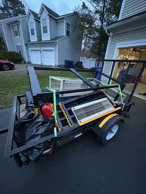 A trailer with a lot of items on it is parked in front of a house.