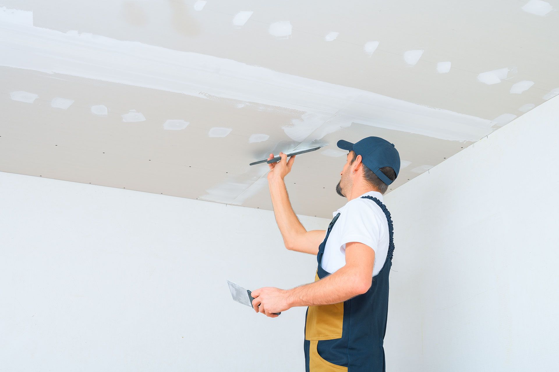 Person taping and smoothing drywall mud on a ceiling with a putty knife