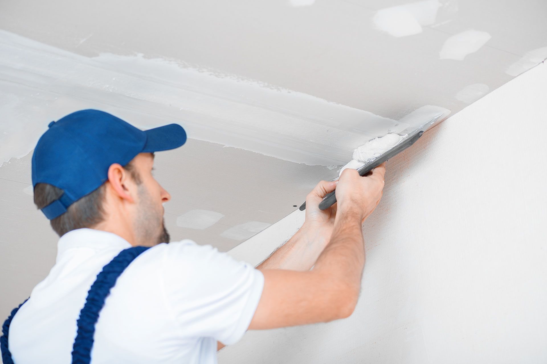 Person in a blue cap applying plaster to a white ceiling with a trowel