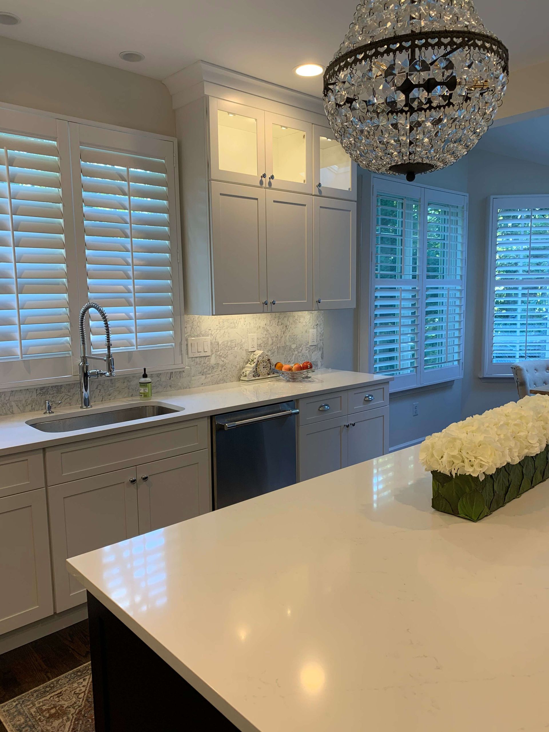 A kitchen with white cabinets , a sink , and a chandelier.