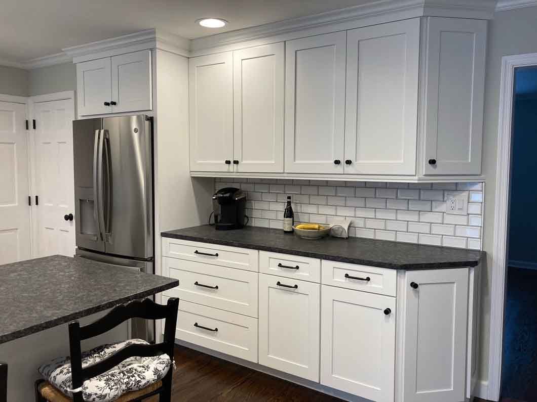 A kitchen with white cabinets , granite counter tops , a refrigerator , and a chair.