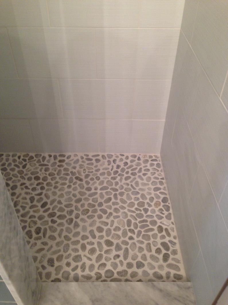 A shower stall with a stone floor and white tiles.