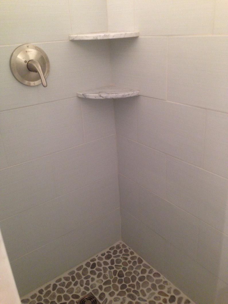 A shower with a corner shelf and a shower head.