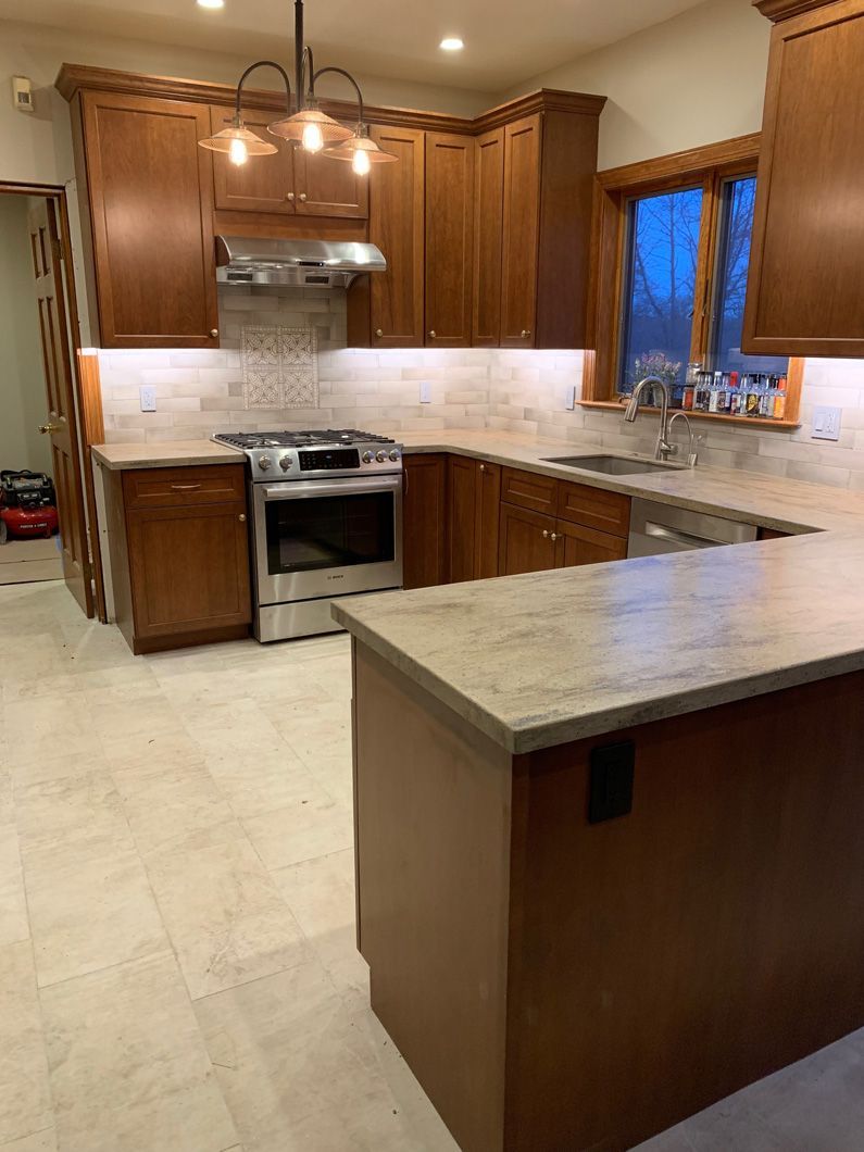 A kitchen with wooden cabinets , a stove , a sink , and a large island.