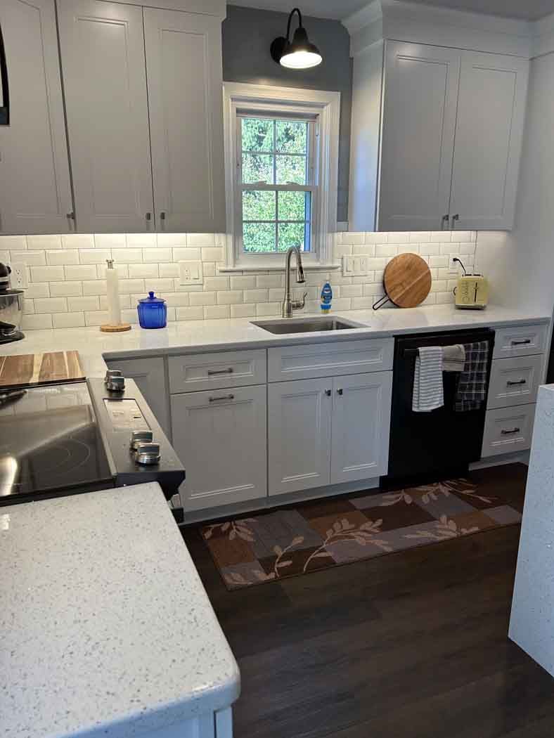 A kitchen with white cabinets , a sink , a stove , and a window.