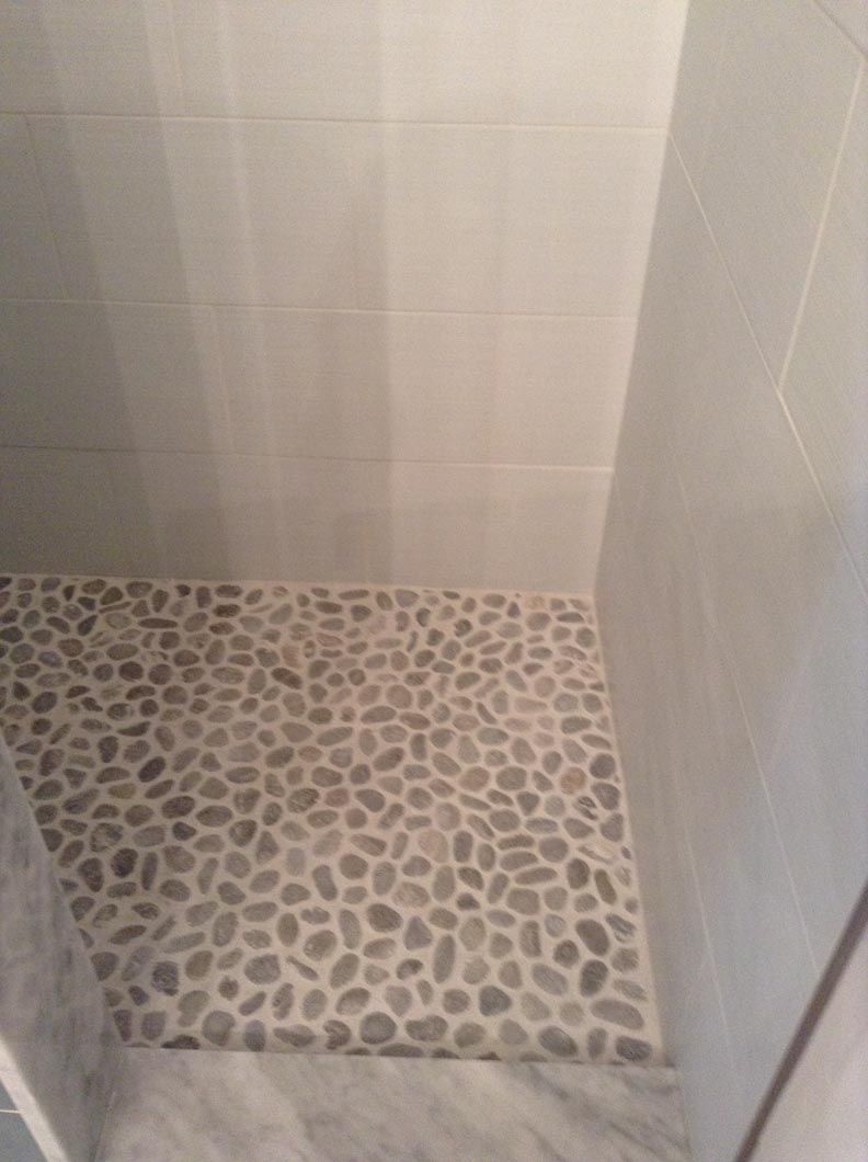 A walk in shower with a tiled floor and a glass door.