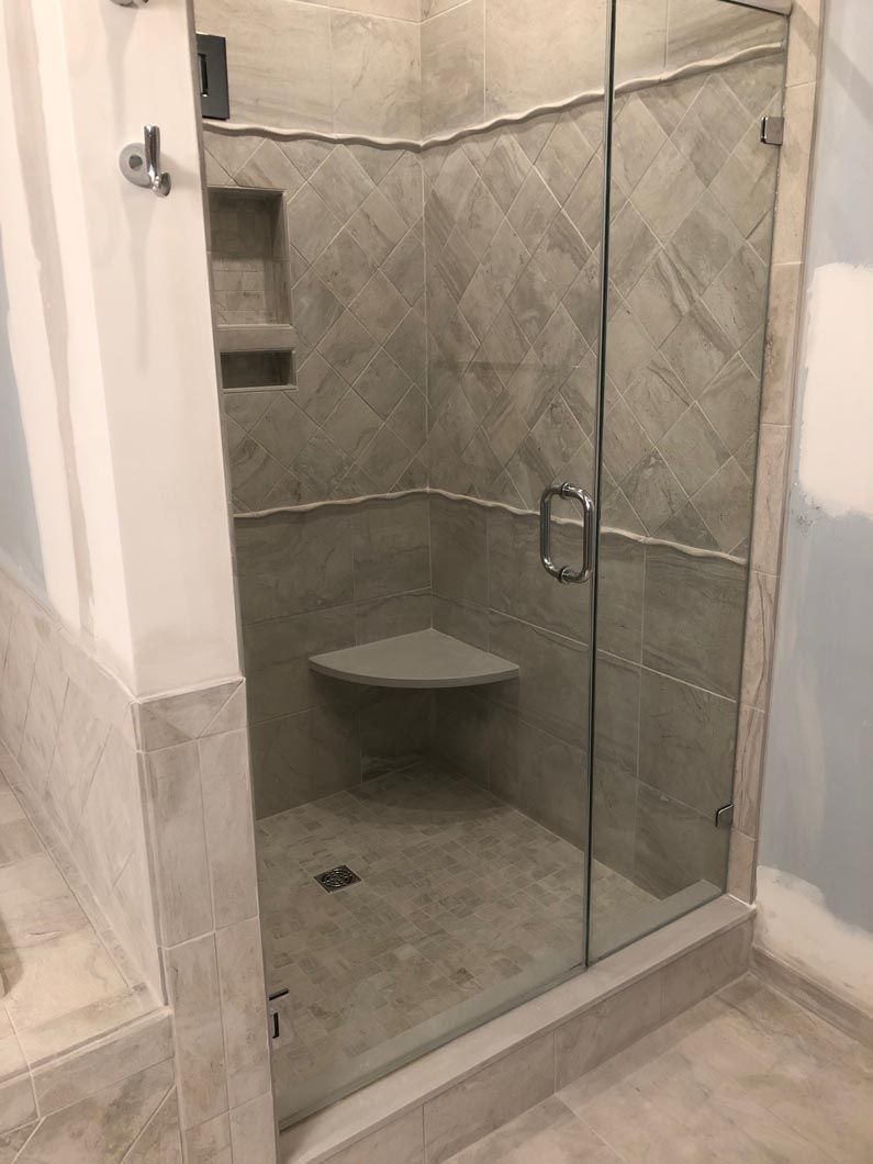 A bathroom with a walk in shower with a glass door and a seat.