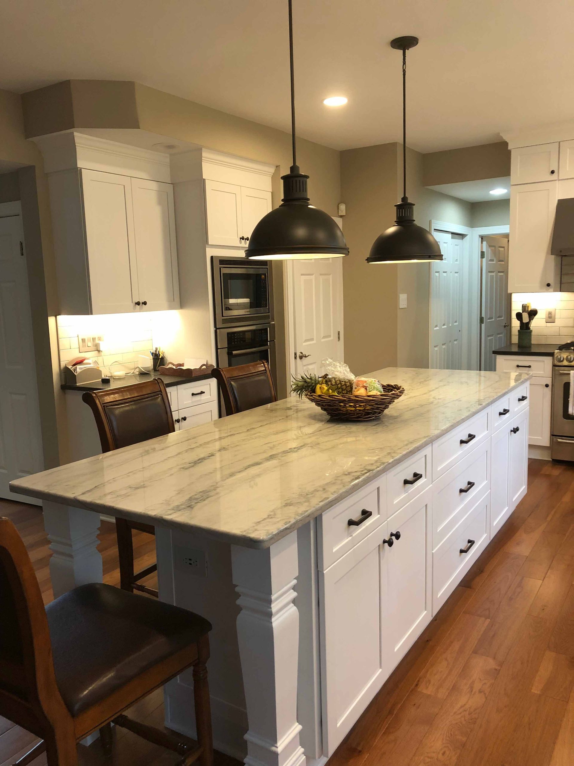 A kitchen with white cabinets and a large island with a bowl of fruit on it.