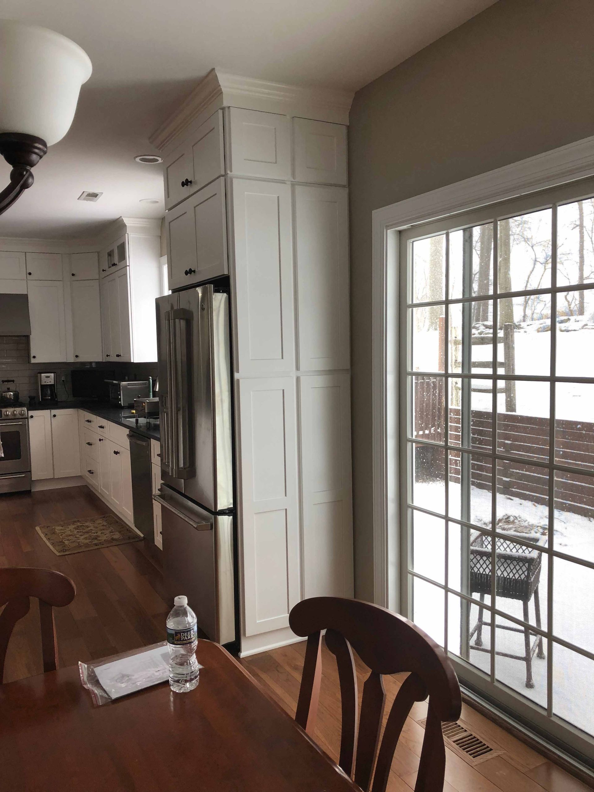 A kitchen with a table , chairs , refrigerator and sliding glass doors.