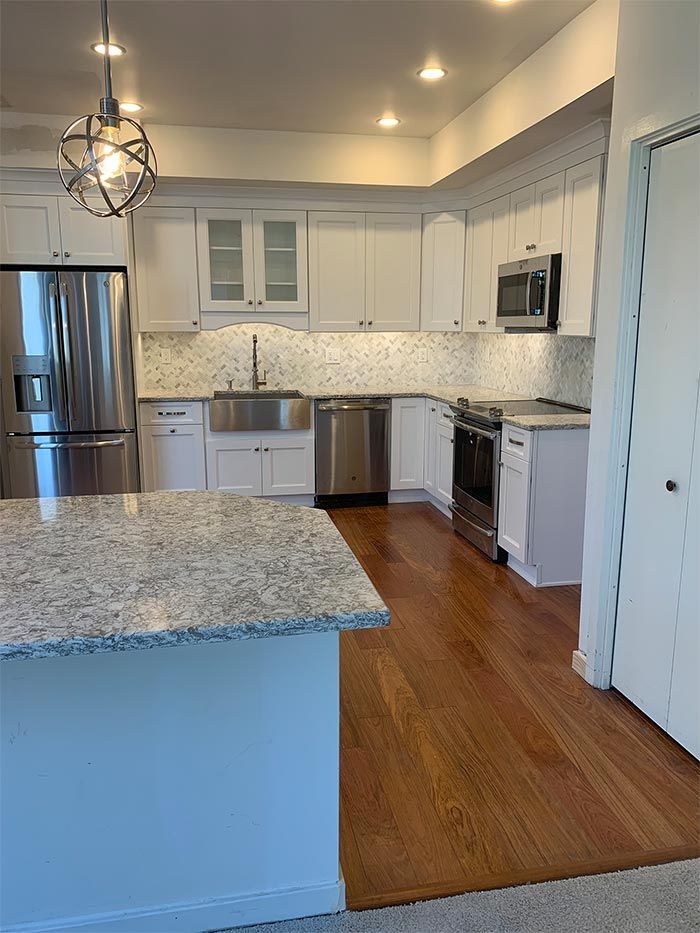A kitchen with white cabinets , stainless steel appliances , granite counter tops and hardwood floors.