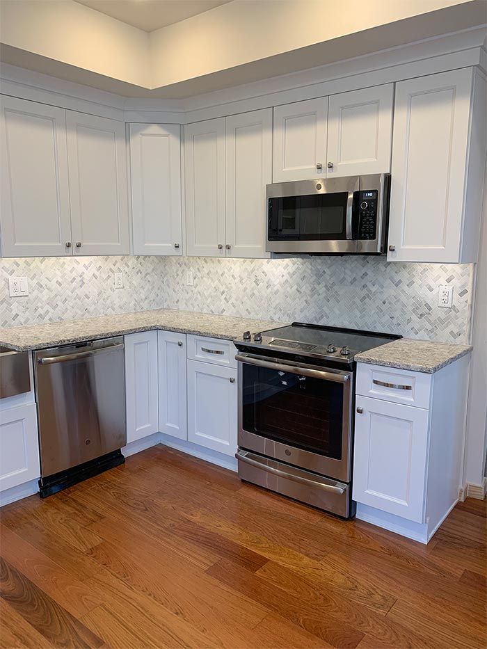 A kitchen with white cabinets , stainless steel appliances , and hardwood floors.