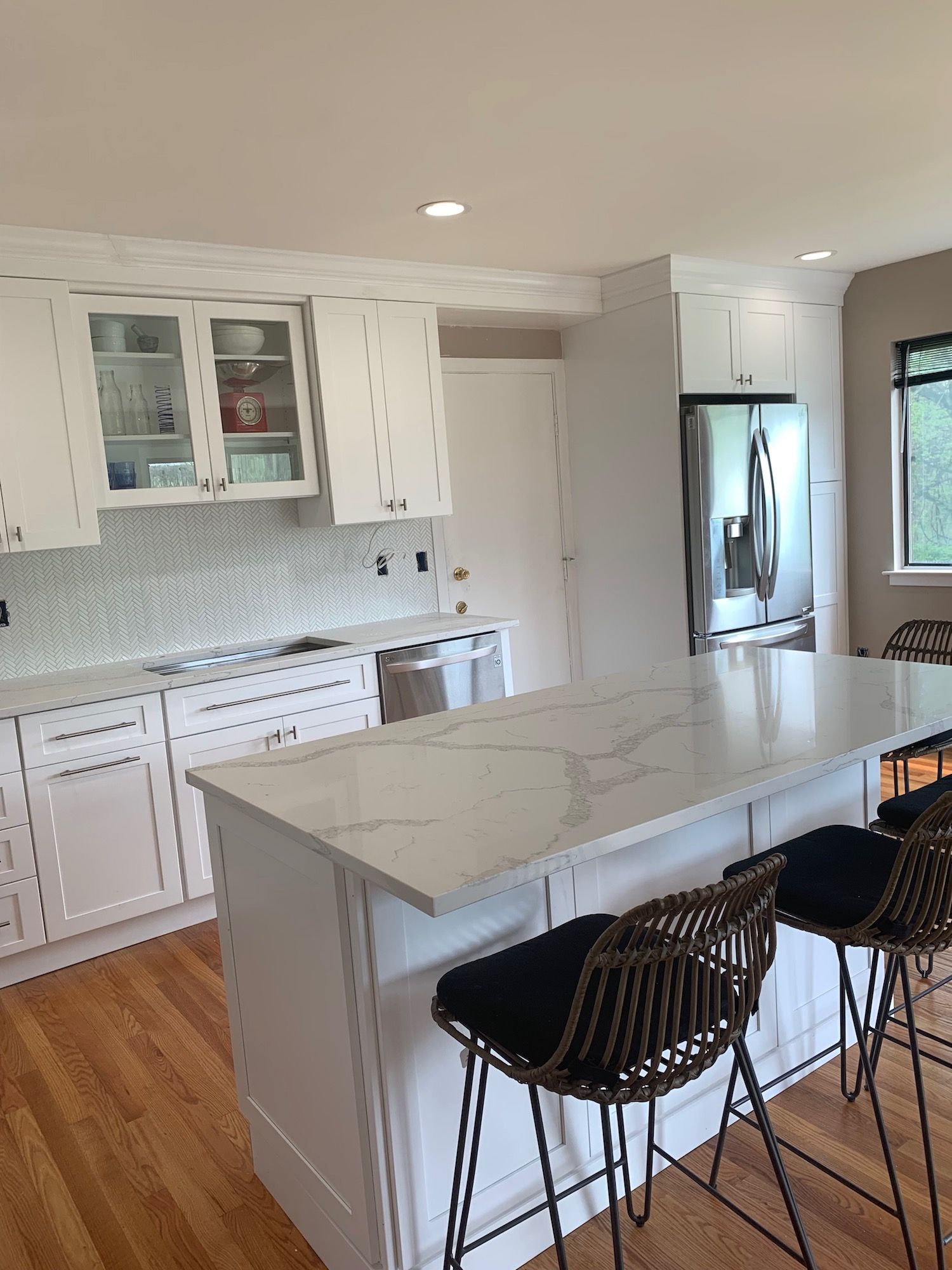 A kitchen with white cabinets , a large island , stools and a refrigerator.