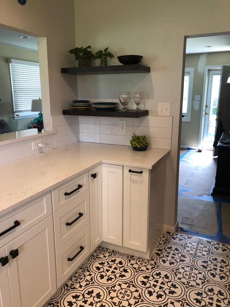 A kitchen with white cabinets and black handles and a black and white tile floor.
