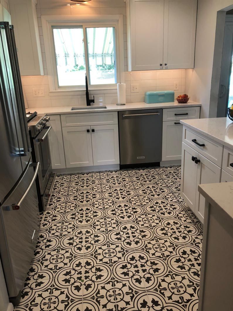 A kitchen with white cabinets , stainless steel appliances , and a black and white tile floor.