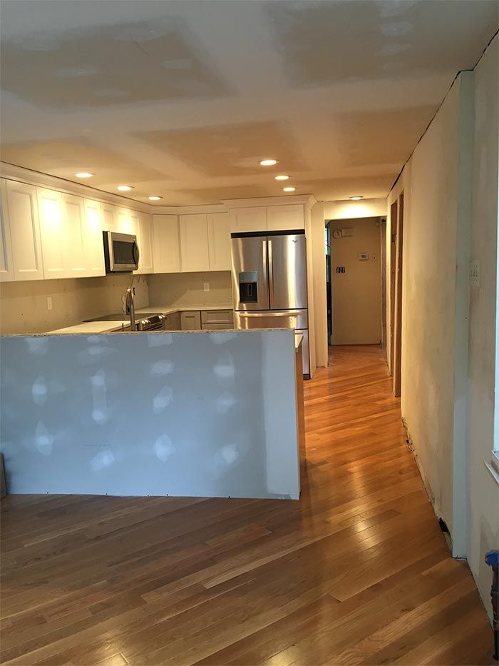 An empty kitchen with hardwood floors and white cabinets.