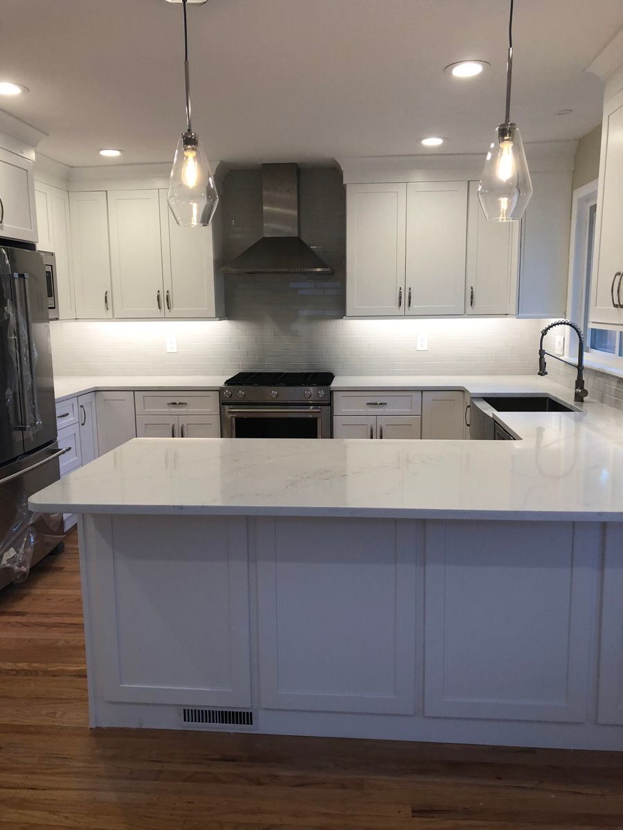 A kitchen with white cabinets , stainless steel appliances , and a large island.
