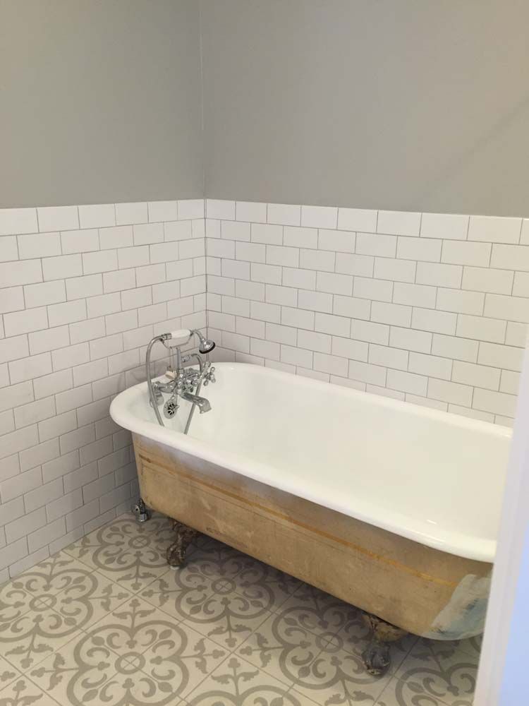 A bathtub in a bathroom with white tiles and a patterned floor.