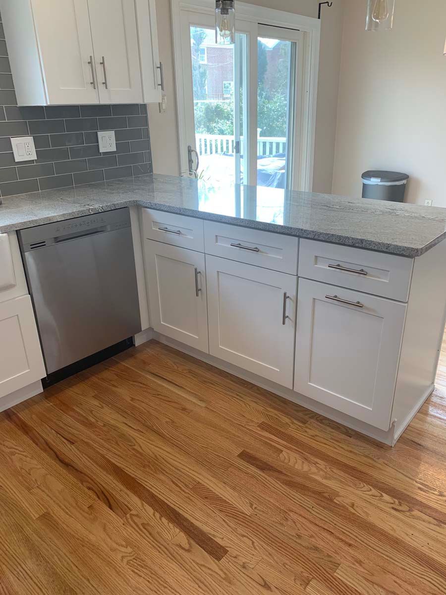 A kitchen with white cabinets , granite counter tops , stainless steel appliances and hardwood floors.