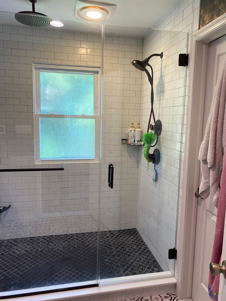 A bathroom with a walk in shower with a glass door and a window.