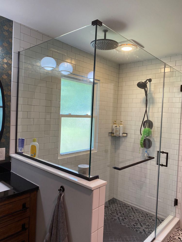 A bathroom with a walk in shower with a glass door and a window.