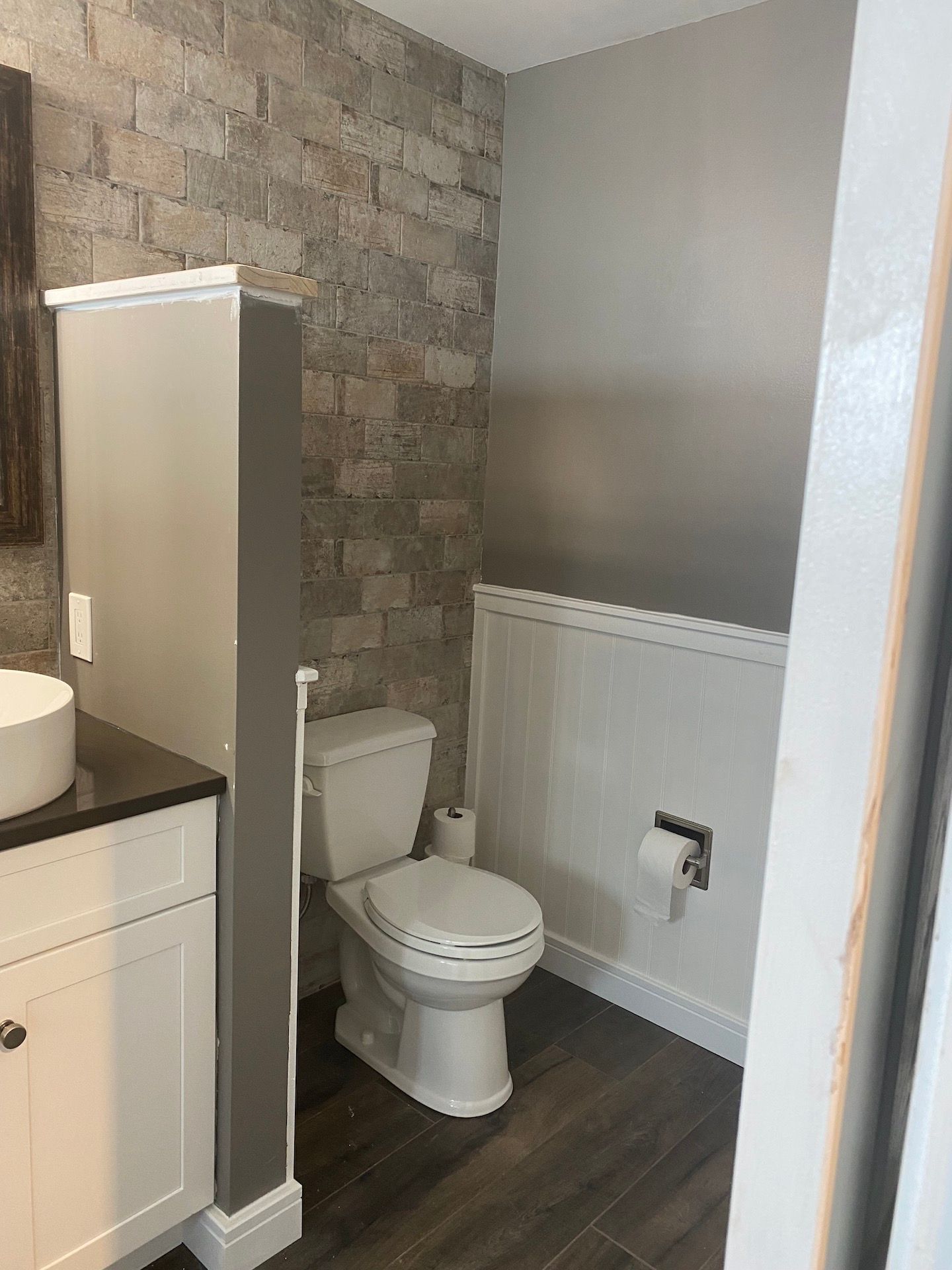 A bathroom with a toilet , sink , and brick wall.