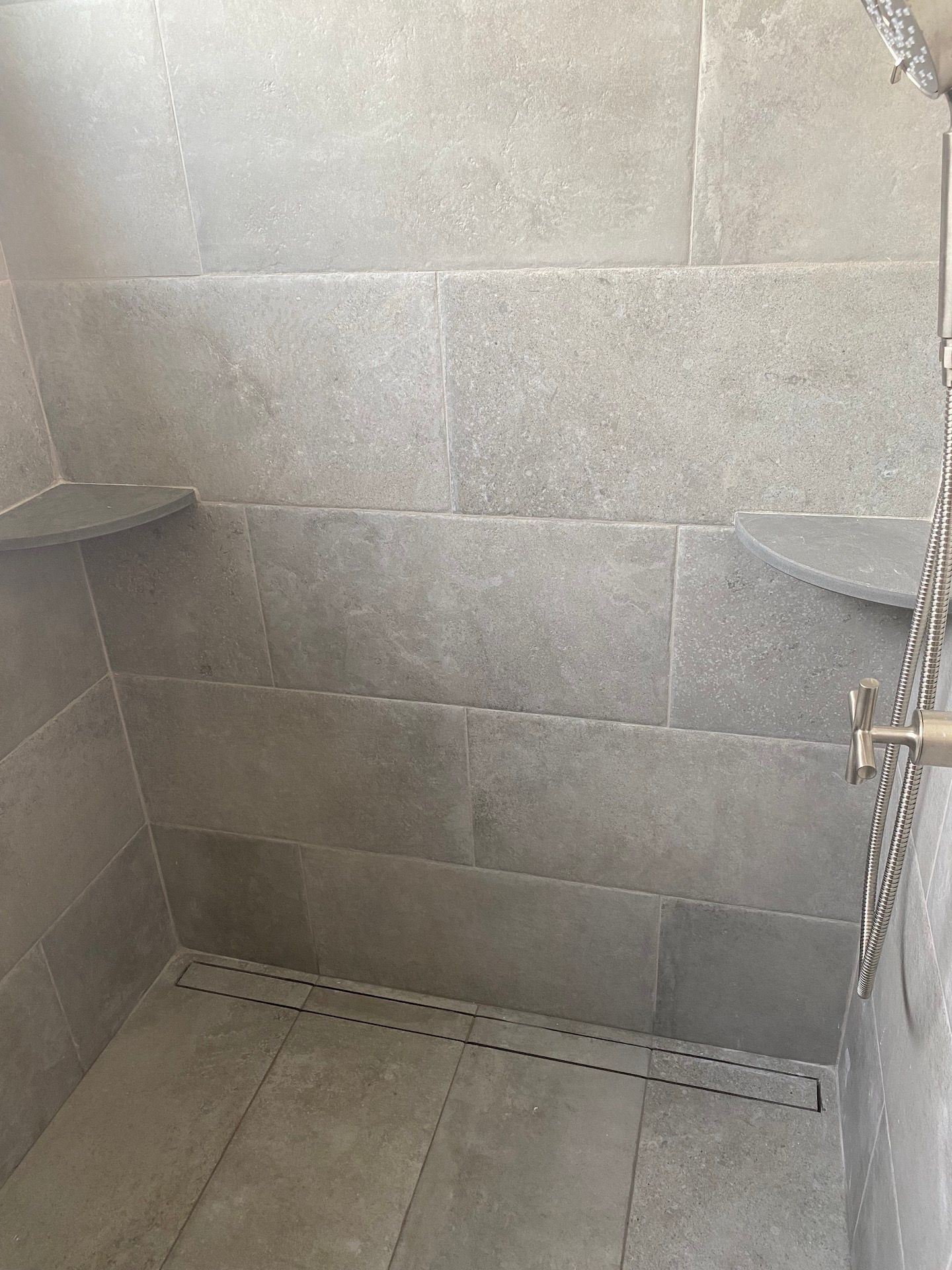 A shower with a drain in the floor and a shelf on the wall.