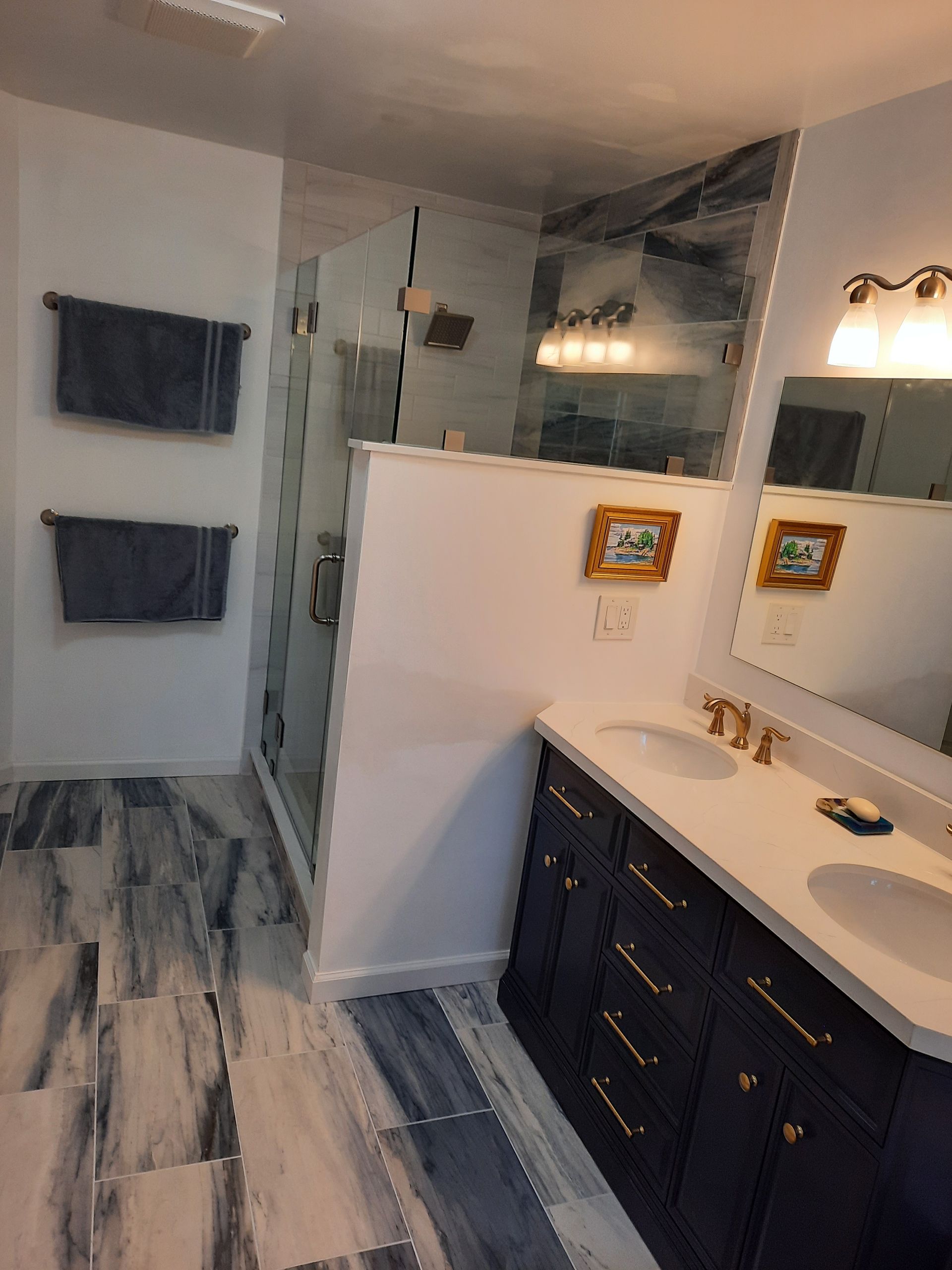 A bathroom with two sinks , a mirror and a walk in shower.